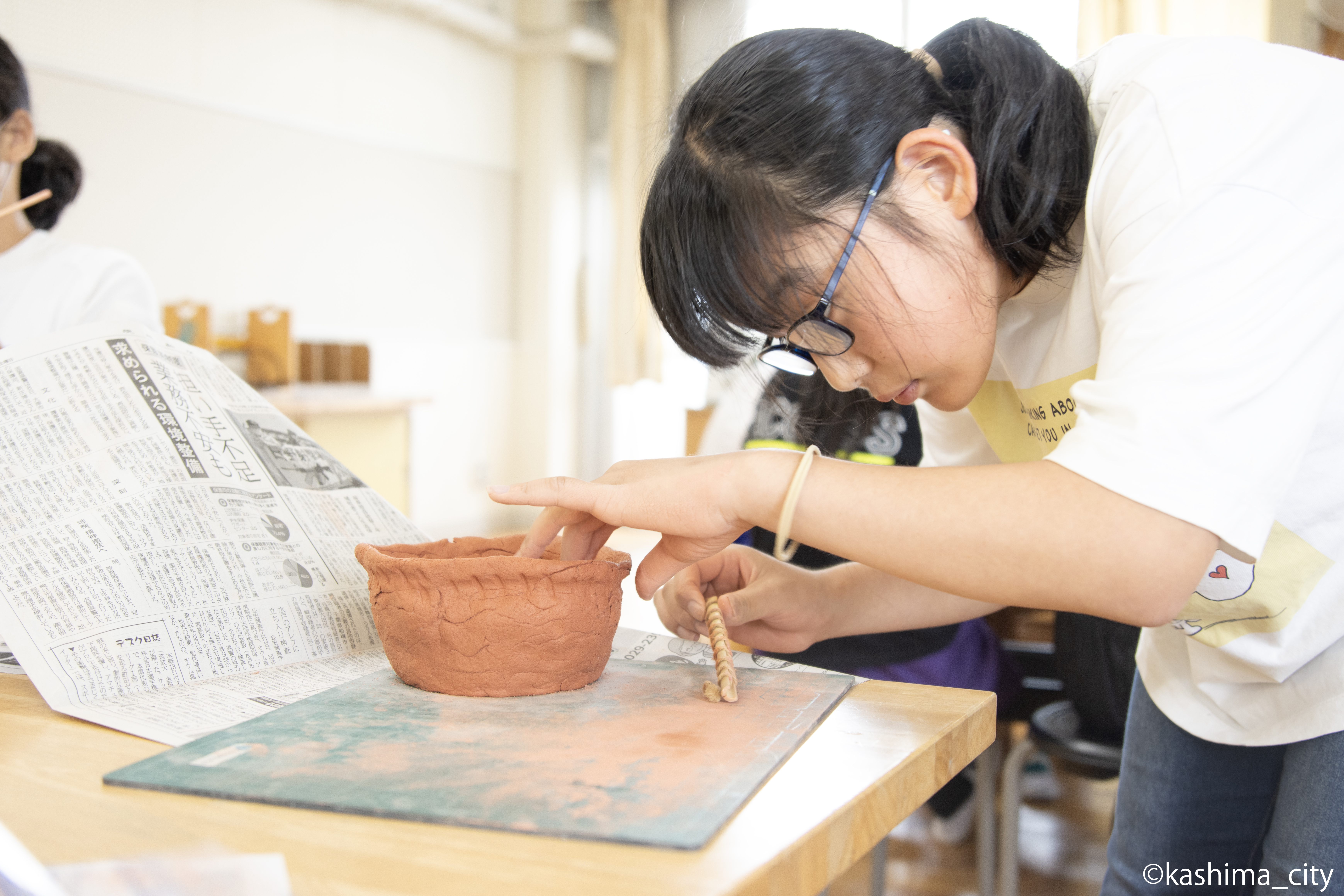 女子児童が土器に縄目の模様をつける様子