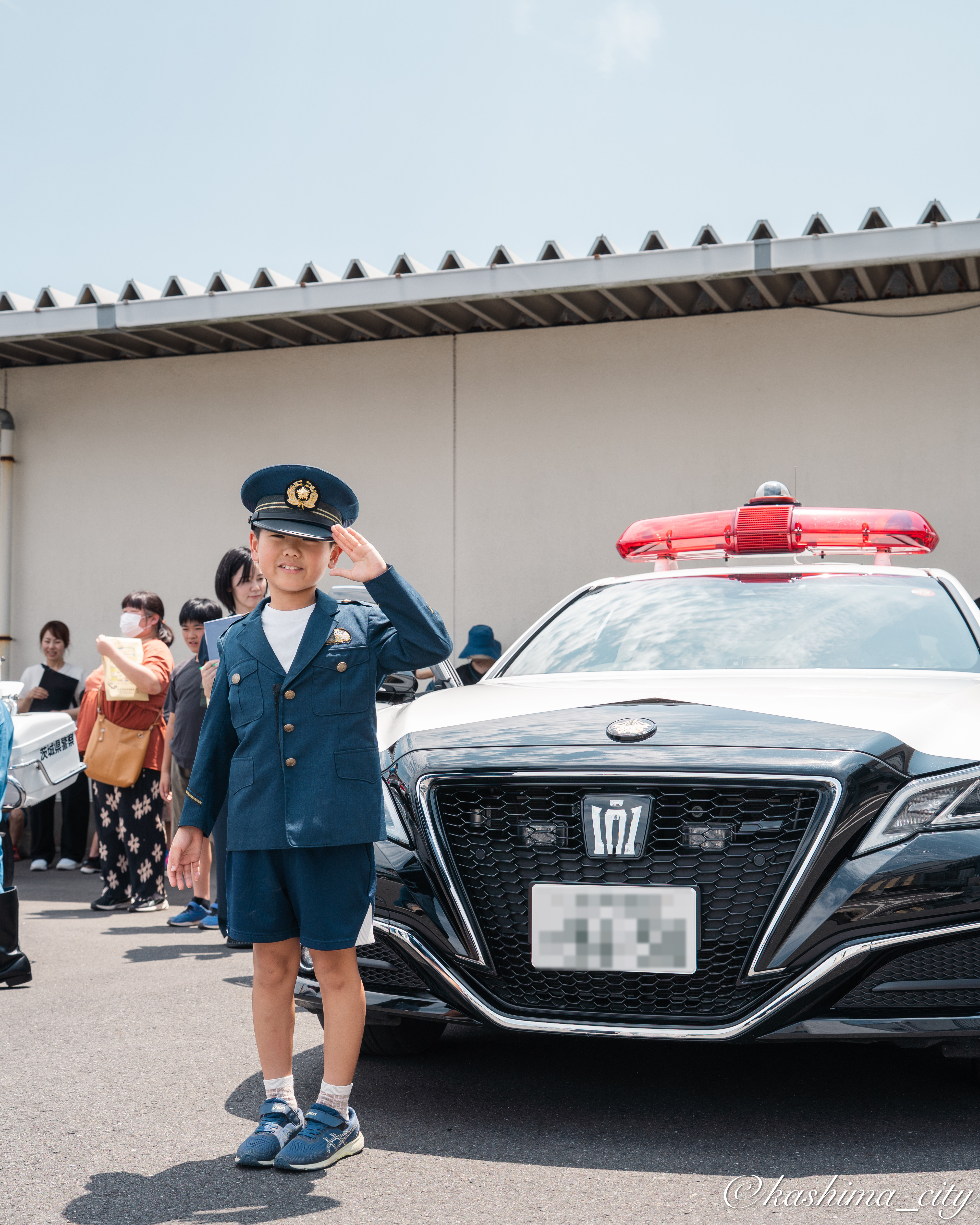 パトカーの前で敬礼をする少年